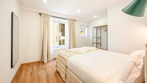 Un dormitorio con cama, ventana con cortinas, mesita de noche, armario y lámpara colgante.