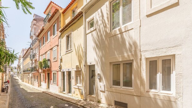 Una calle empedrada flanqueada por edificios de varios pisos, algunos con balcones y contraventanas.