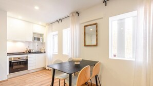 Una cocina moderna con armarios blancos, un microondas y un tostador. Hay una mesa de comedor con sillas y un espejo grande en la pared.