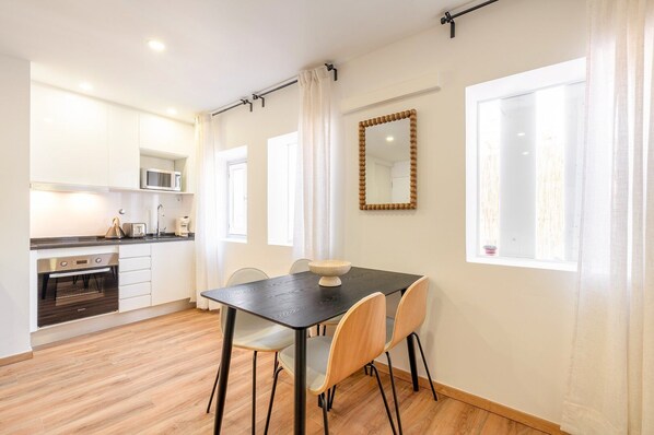 A modern kitchen with white cabinets, a microwave, and a toaster. There is a dining table with chairs and a large mirror on the wall.