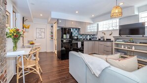A modern kitchen with a refrigerator, microwave, and stove. There is a dining area with a table and chairs, and a sofa in the living room.