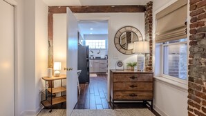 A hallway with a wooden dresser, a mirror, and a window with blinds.