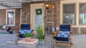 A brick building with two wooden chairs with blue cushions, a glass table, and a potted plant.