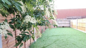 A backyard with artificial grass, a wooden fence, and a tree with white flowers.