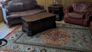 Ein Wohnzimmer mit braunem Ledersofa, einem passenden Sessel, einem Holztisch und einem gemusterten Teppich.