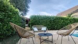 A patio with two wicker chairs and a small table, surrounded by stone tiles and greenery.