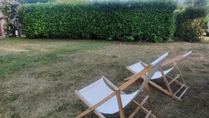 A grassy outdoor area with two wooden chairs and a stone building in the background.