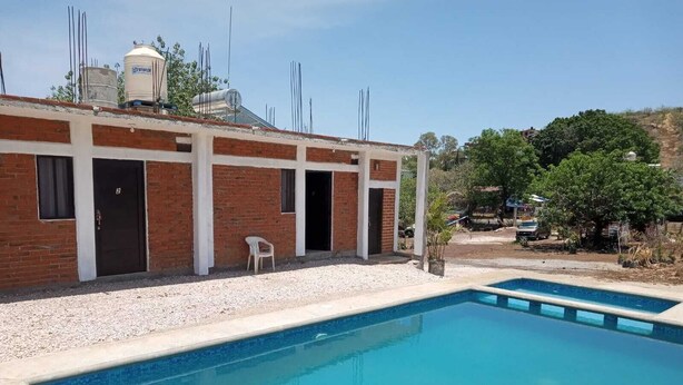 Une piscine située à côté d’un bâtiment dont la façade est en briques et qui possède plusieurs portes.