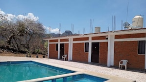 Un bâtiment situé au bord de la piscine, avec une façade en briques, deux portes et un réservoir d’eau sur le toit.