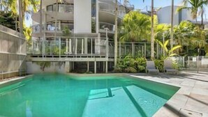 A swimming pool with a clear blue water, surrounded by a fence and palm trees.