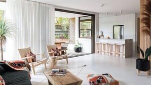 A modern living room with a sofa, chairs, and a coffee table. There is a kitchen area with bar stools and a refrigerator.