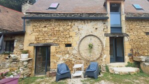 A stone building with a small porch, two chairs, and a potted plant. - Private Jacuzzi, F2 garden apartment + separate rupestral room. Near Sarlat (Carsac-Aillac)