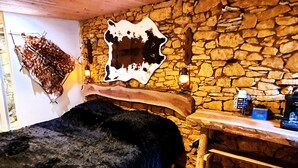 A rustic room with a stone wall, a wooden bed, and a mounted animal hide. - Private Jacuzzi, F2 garden apartment + separate rupestral room. Near Sarlat (Carsac-Aillac)
