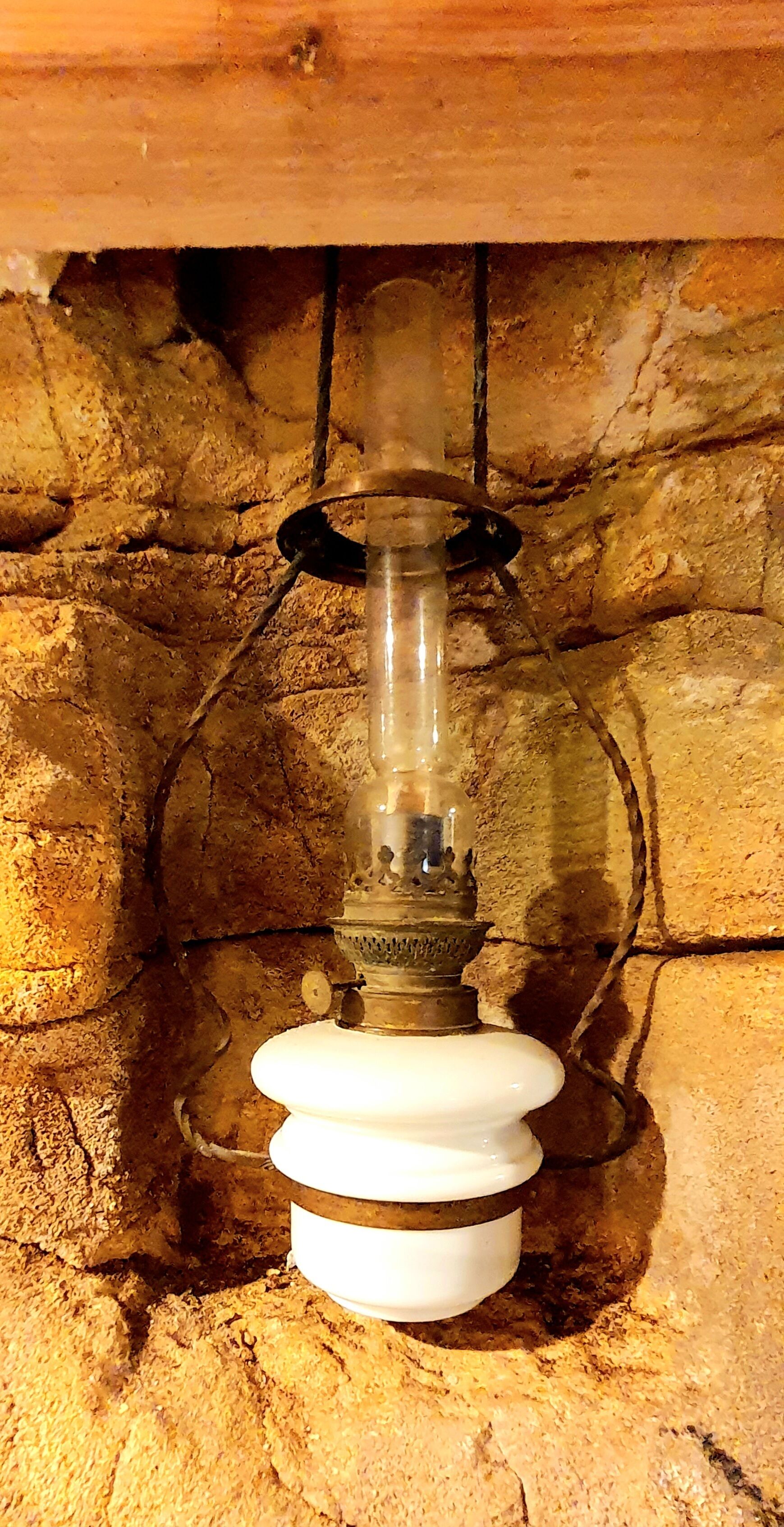 Eine antike Wasserpumpe mit einem durchsichtigen Glasbehälter vor einer rustikalen Steinwand.