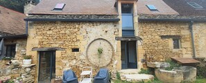 A stone building with a small porch, two chairs, and a potted plant. - Private Jacuzzi, F2 garden apartment + separate rupestral room. Near Sarlat (Carsac-Aillac)