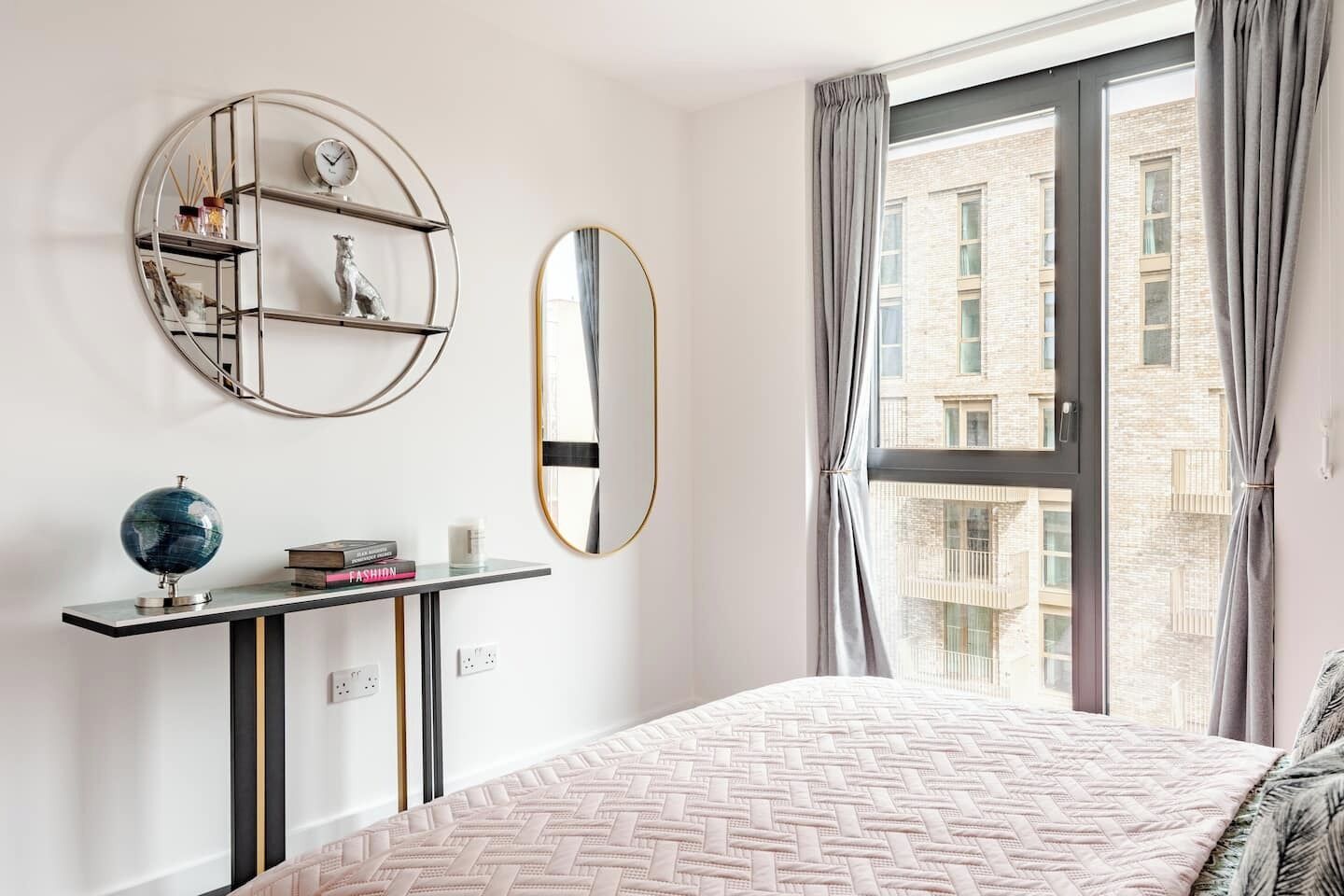 A bedroom with a bed, a round mirror, a globe, and a shelf with books and decorative items.