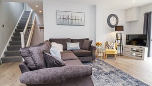 A modern living room with a sectional sofa, a flat-screen TV, a staircase, and a painting on the wall. - Beach Hideaway (Bideford)