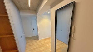 A hallway with a wooden staircase, a large mirror, and a door leading to another room.