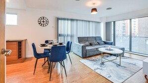 A modern living room with a dining area, a grey sofa, a round coffee table, and a large window offering a city view. - City Retreat in Manchester (Manchester)