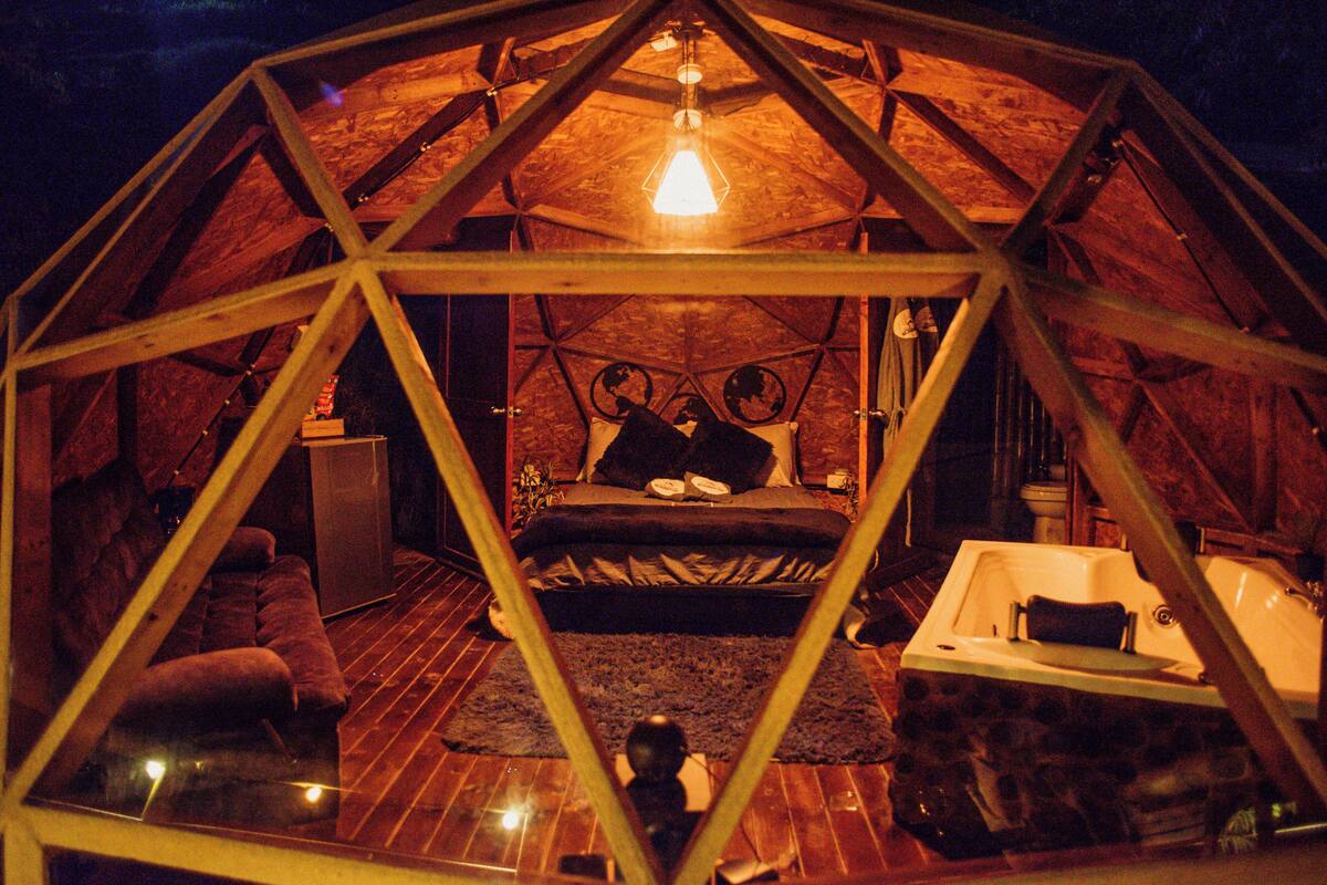 Een geodetische koepelstructuur met een bed, een badkuip en een klein tafeltje.