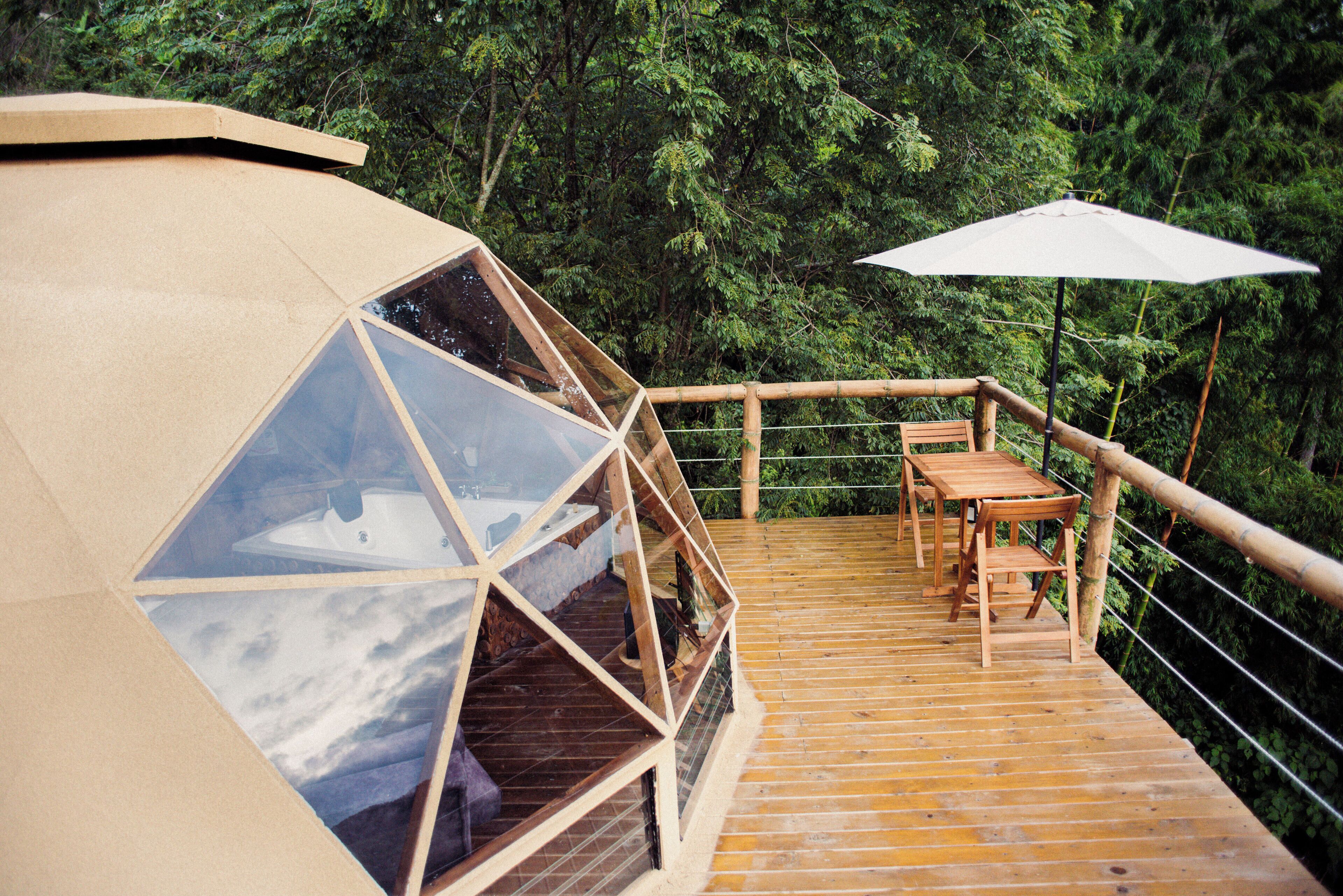 A wooden deck with a glass-enclosed structure, a table, chairs, and an umbrella.