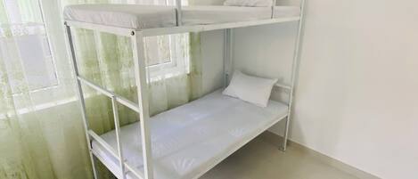 A bunk bed in a room with a window and sheer curtains.