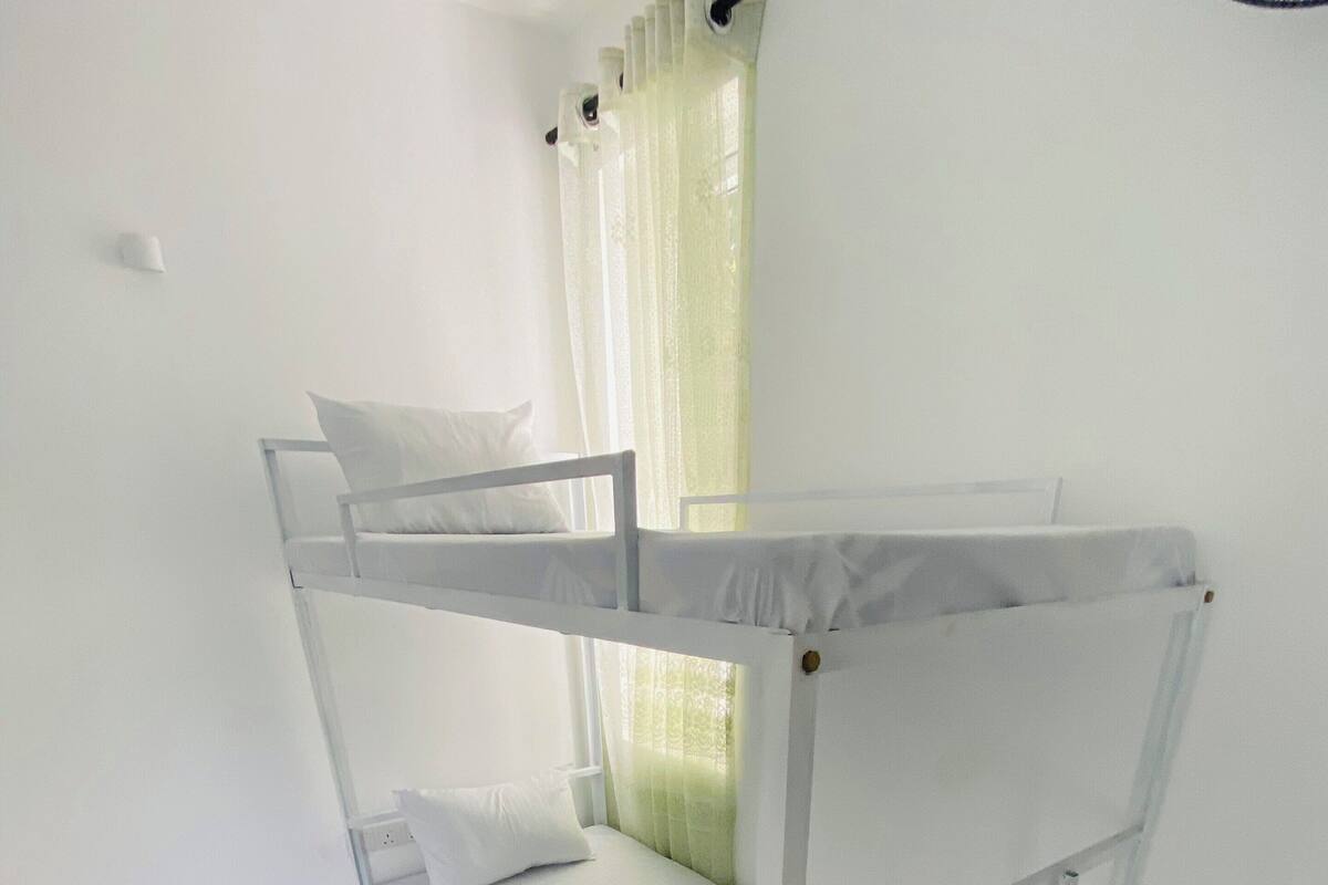 A bunk bed with white bedding and a window with a curtain.