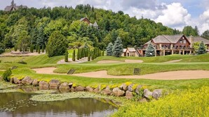 A golf course with a pond, a clubhouse, and surrounding trees.