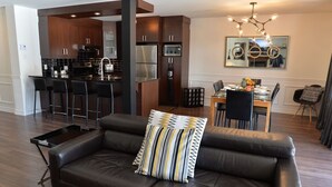 A modern living room with a leather sofa, a dining area, and a kitchen with dark wood cabinets and stainless steel appliances.