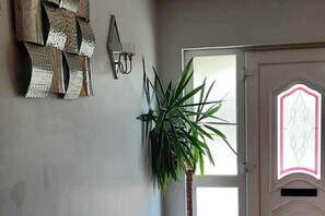 Una habitación con una planta grande en maceta, un espejo adosado a la pared y una puerta con un panel de vidrio decorativo.