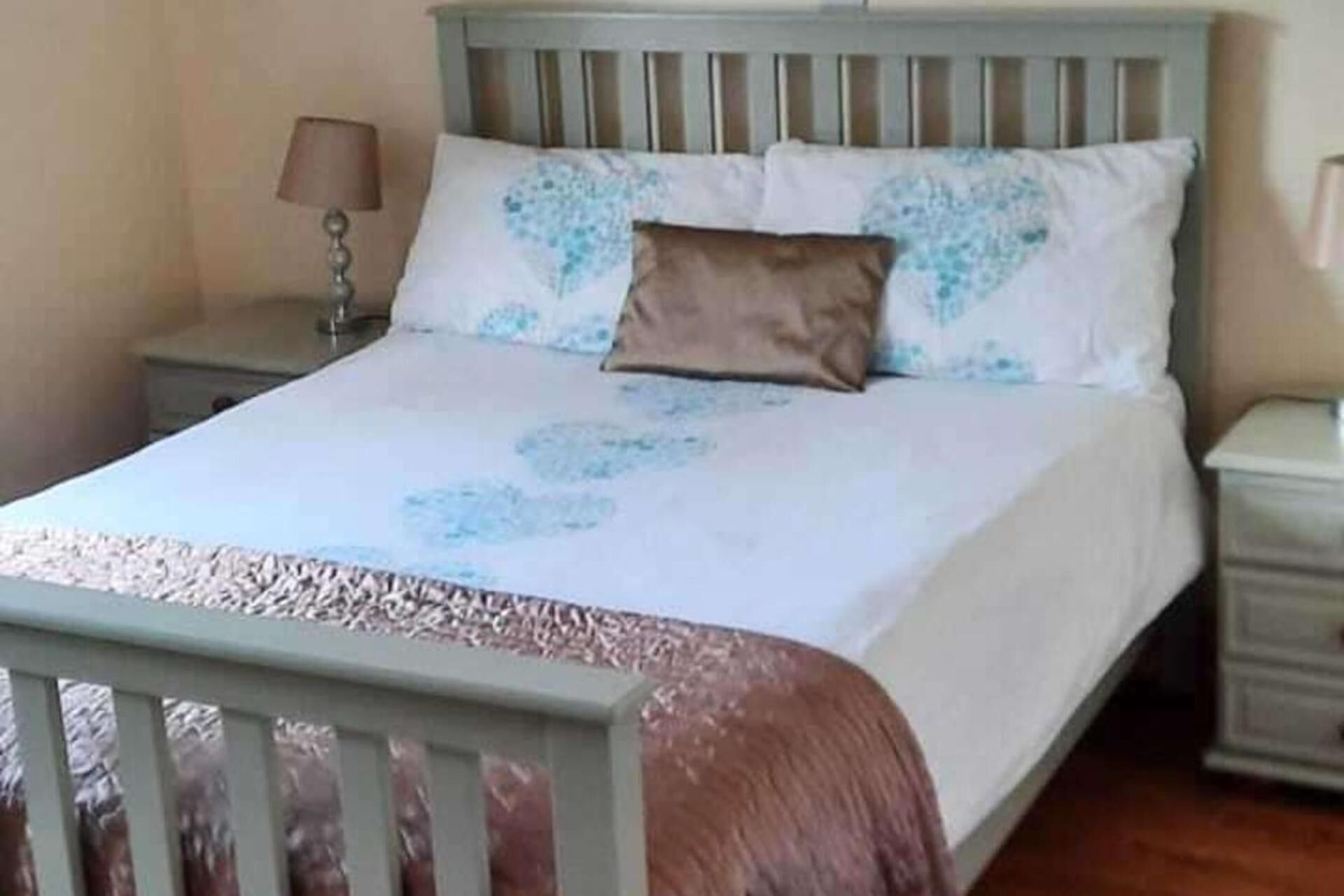 Een bed met een wit en blauw bloemenbedekking, een bruin kussen en een houten hoofdeinde.