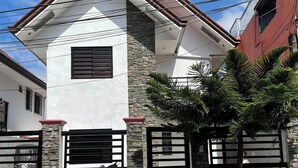 Une maison à deux étages avec une façade en pierre, un petit jardin à l’avant et un portail en métal.