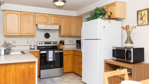 A modern kitchen with wooden cabinets, stainless steel appliances, and a small dining area. - Pacific Drift at Proposal Rock w/Beach Access (Neskowin)