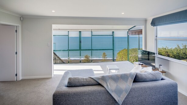 Un dormitorio moderno con un ventanal grande que da al mar, un sofá gris y una mesita de noche con una lámpara.