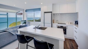 Una cocina moderna con una isla grande, armarios blancos y vista al mar.