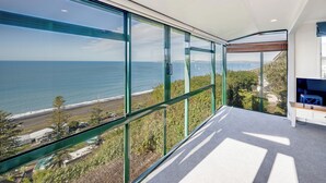 Habitación moderna con amplios ventanales desde el suelo hasta el techo que ofrecen vistas al mar y a la playa.
