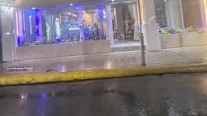 A bar and lounge with a neon sign, outdoor seating, and a wet pavement.