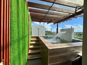 Un espace moderne aménagé à l’extérieur avec un jacuzzi, une pergola en bois, une pelouse artificielle et une vue sur un quartier résidentiel.