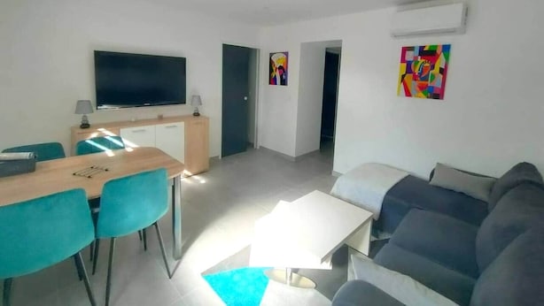 Moderni olohuone, jossa on sohva, ruokailutila pöytineen ja tuoleineen sekä seinälle asennettu televisio.