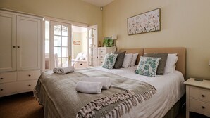 Un dormitorio con una cama grande, una mesita de noche, un aparador y una puerta que da a otra habitación.