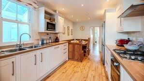 Una cocina moderna con armarios blancos, una mesa de comedor de madera, un tostador rojo y una estufa a gas.