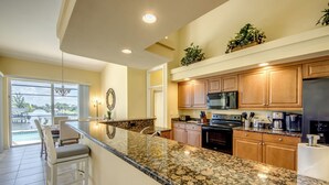 A kitchen with granite countertops, wooden cabinets, a stainless steel refrigerator, and a built-in microwave. - Heated Pool - Dock - Gulf Access Canal - BBQ (Cape Coral)