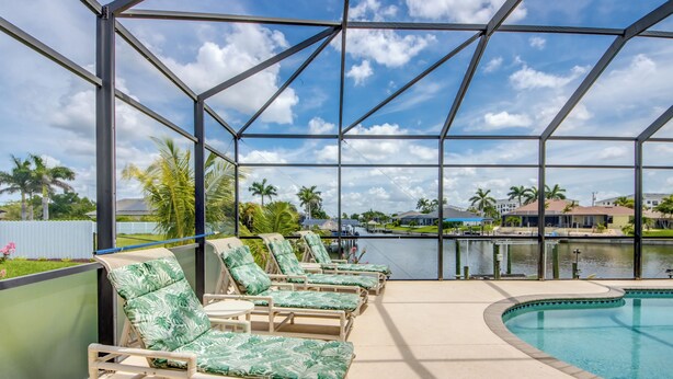 A poolside area with lounge chairs and a view of a body of water and palm trees. - Heated Pool - Dock - Gulf Access Canal - BBQ (Cape Coral)