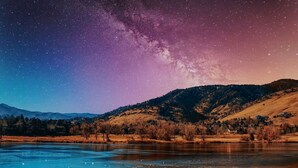 Un paysage nocturne avec un ciel étoilé, une rivière et des collines ondulantes.