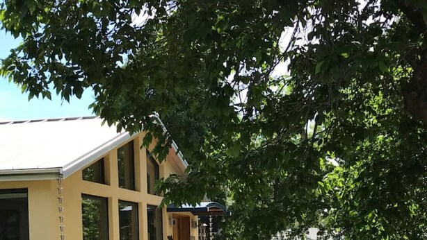 Un bâtiment doté de grandes fenêtres, d’un espace extérieur couvert et d’un jardin agrémenté de sentiers et de mobilier de jardin.