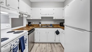 Une cuisine de taille réduite, avec des meubles blancs, une cuisinière, un lave-vaisselle et un réfrigérateur.