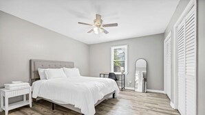 Une chambre à coucher comprenant un lit, un bureau, une chaise, un ventilateur de plafond et une fenêtre.