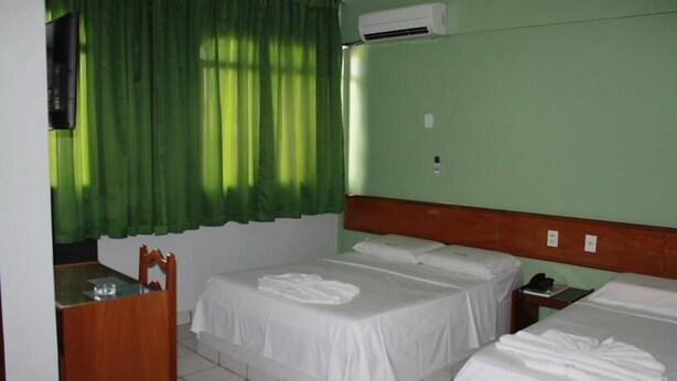 Habitació d'hotel amb dos llits, una nitzeta de fusta, un mirall i una cortina verda.