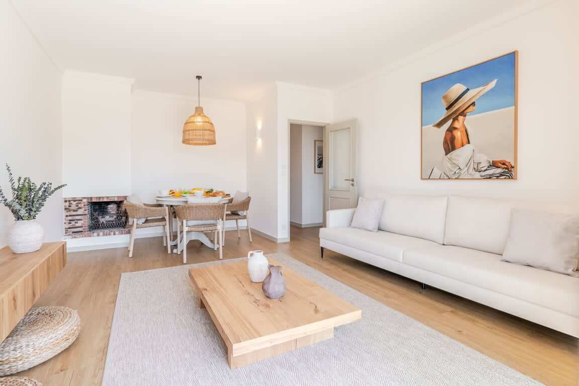 A modern living room with a white sofa, wooden coffee table, and a painting of a person in a hat.