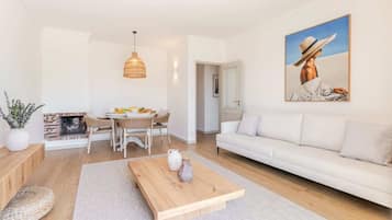 A modern living room with a white sofa, wooden coffee table, and a painting of a person in a hat.